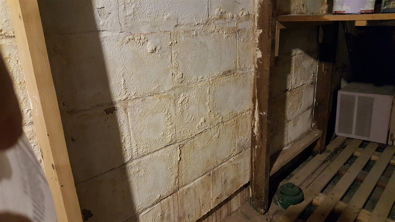 Basement concrete block wall with water damage and wooden support beams.