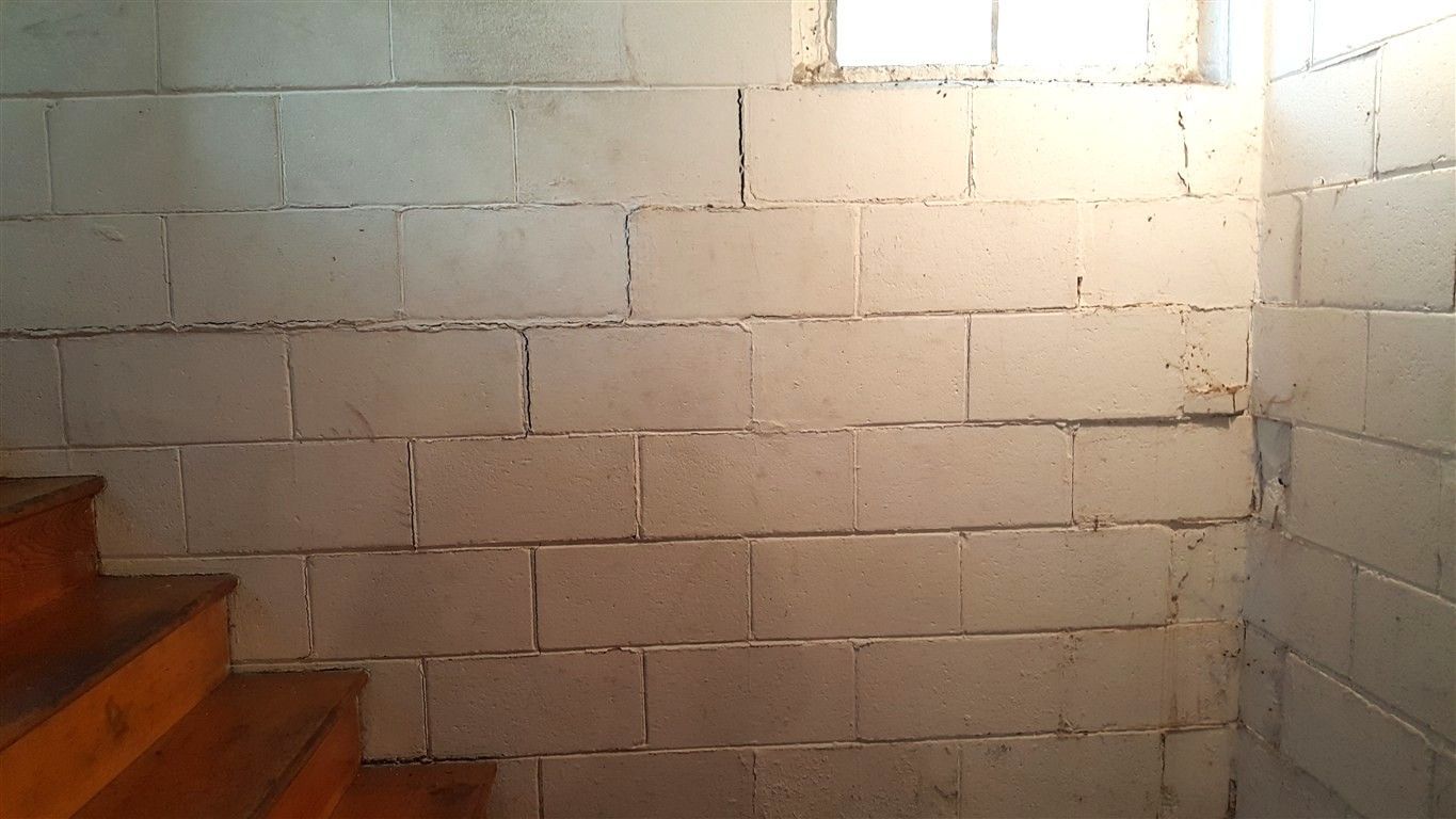 Concrete block wall in a basement, with a small window and wooden stairs on the left.