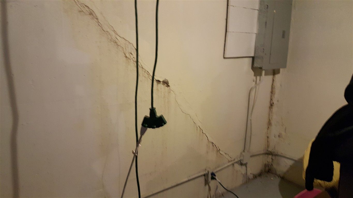 Cracked basement wall with water stains. Electrical box and cords present.