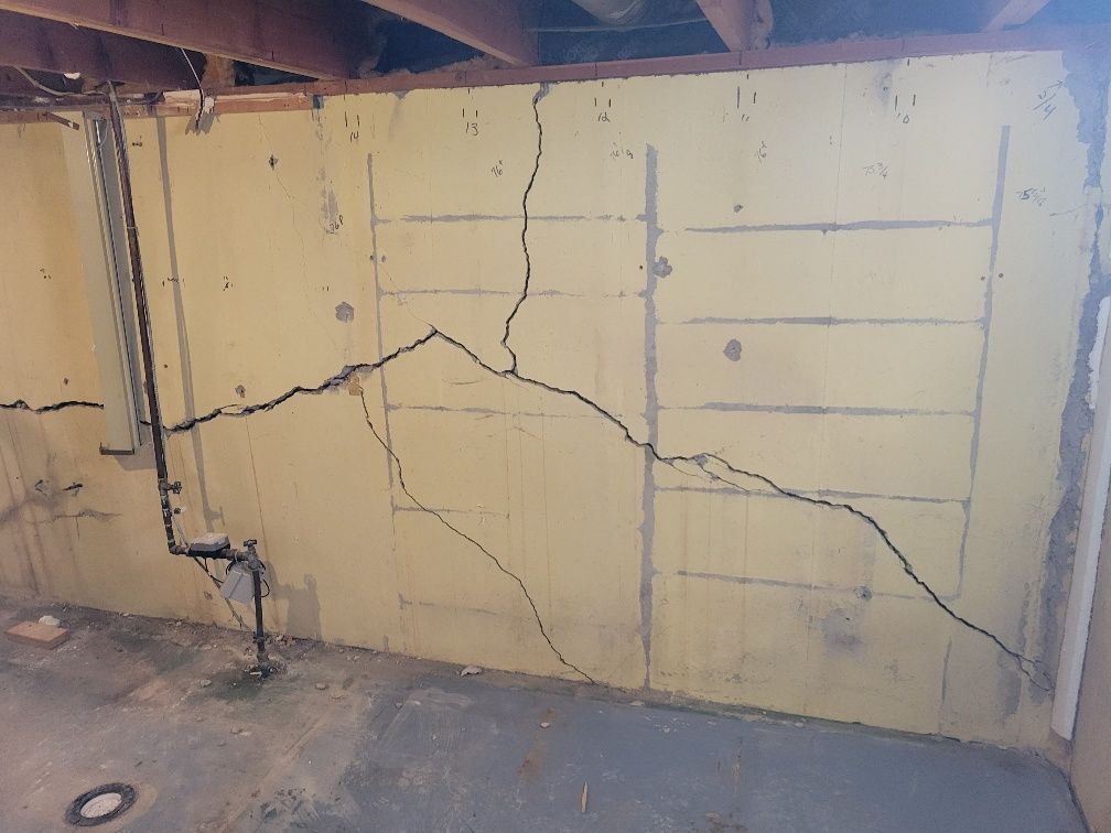 Cracked basement wall painted yellow, with visible horizontal and vertical support lines.