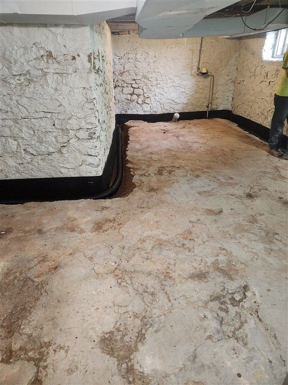 Basement interior with black drainage system installed along the walls, covered with a layer of granular material.