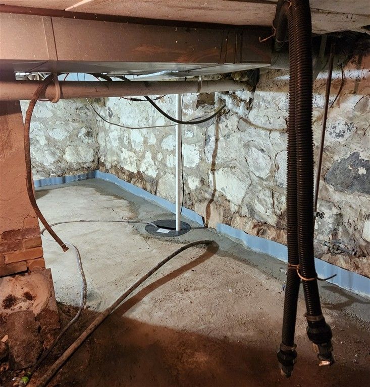Basement with stone walls and concrete floor, sump pump, and drainage system installation.