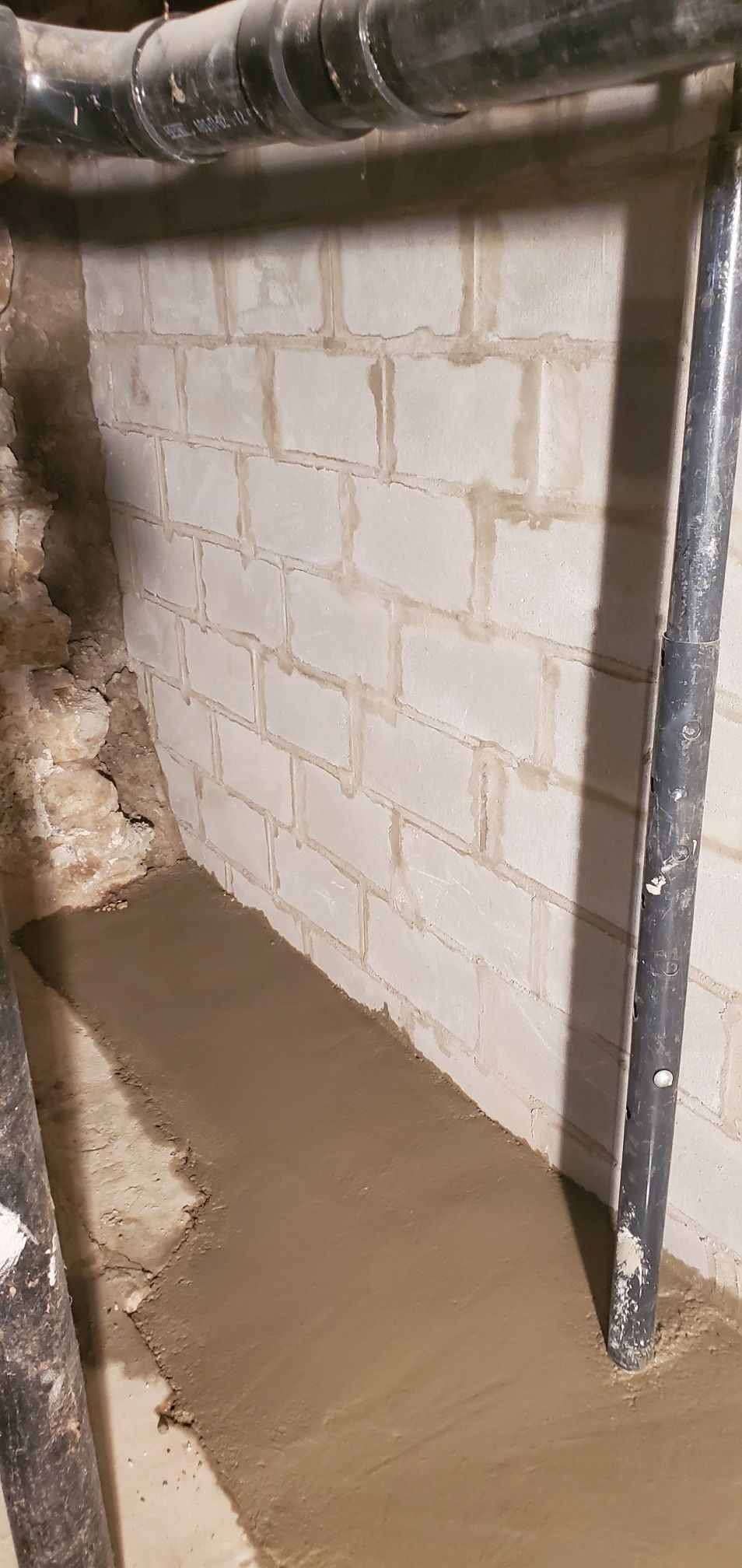 Basement wall with cinder blocks, pipes, and wet concrete floor.