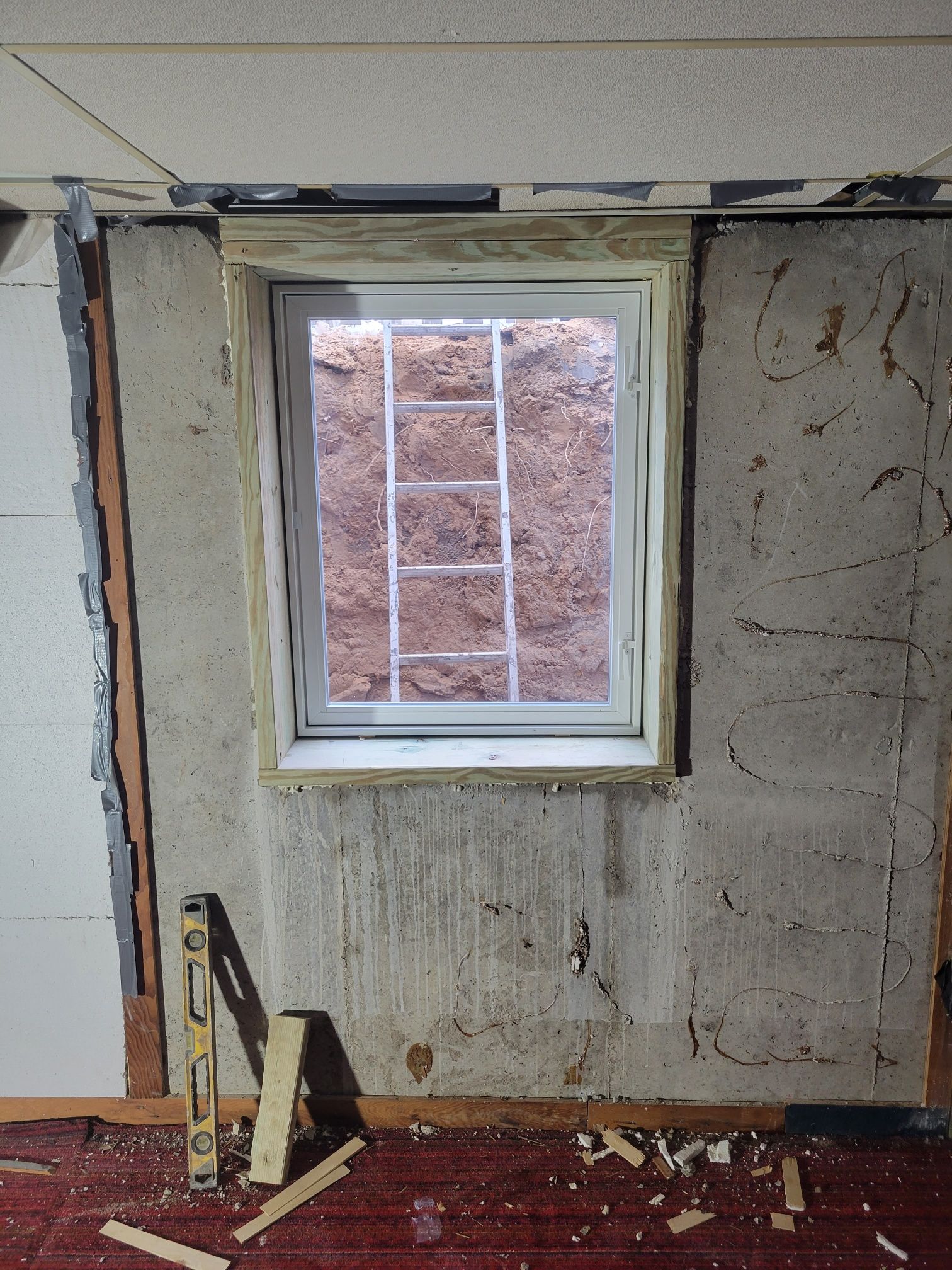 Window frame in a partially demolished basement wall, with a dirt view and tools.