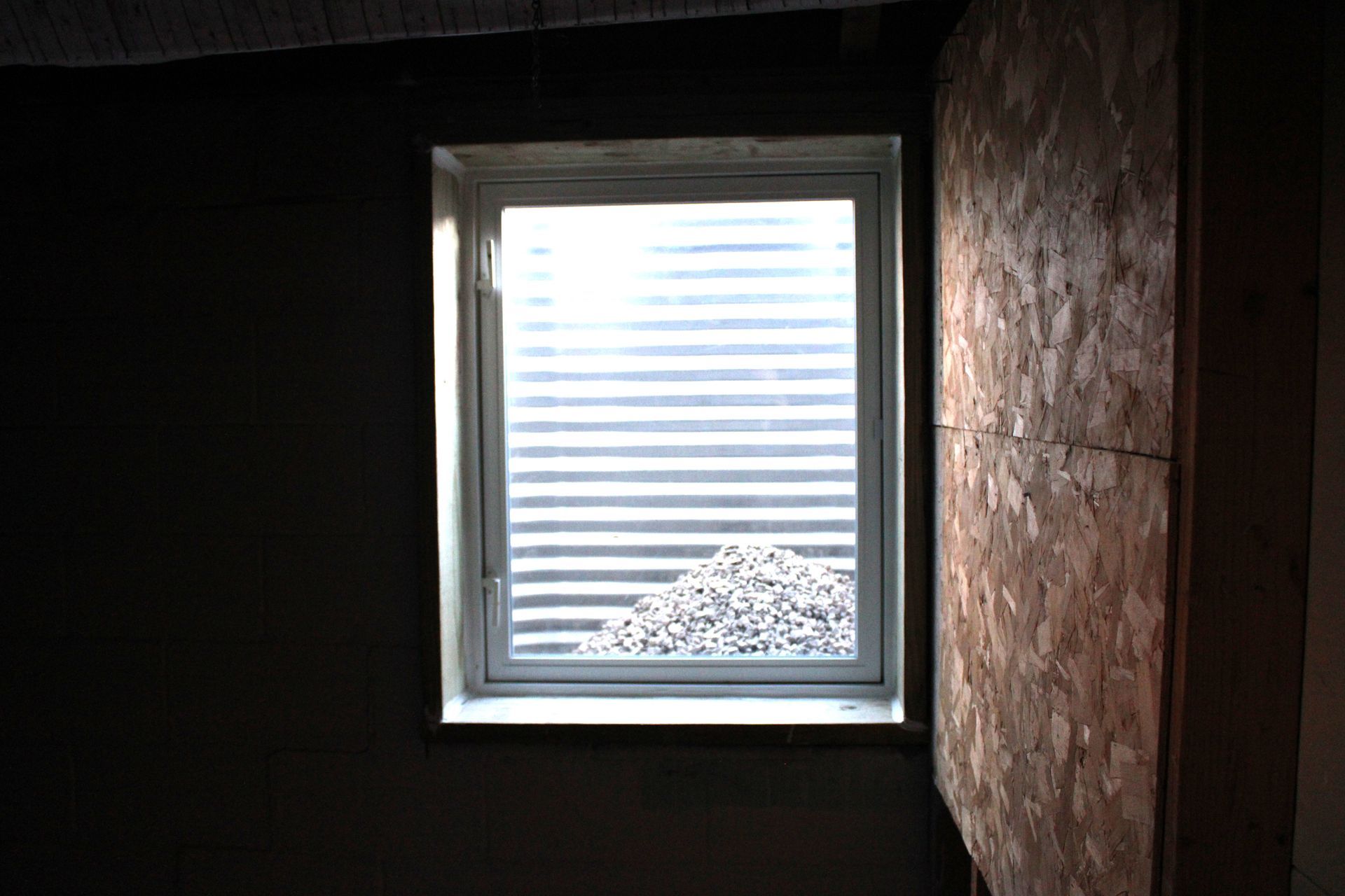 Window in a dark room, overlooking a window well filled with rocks.