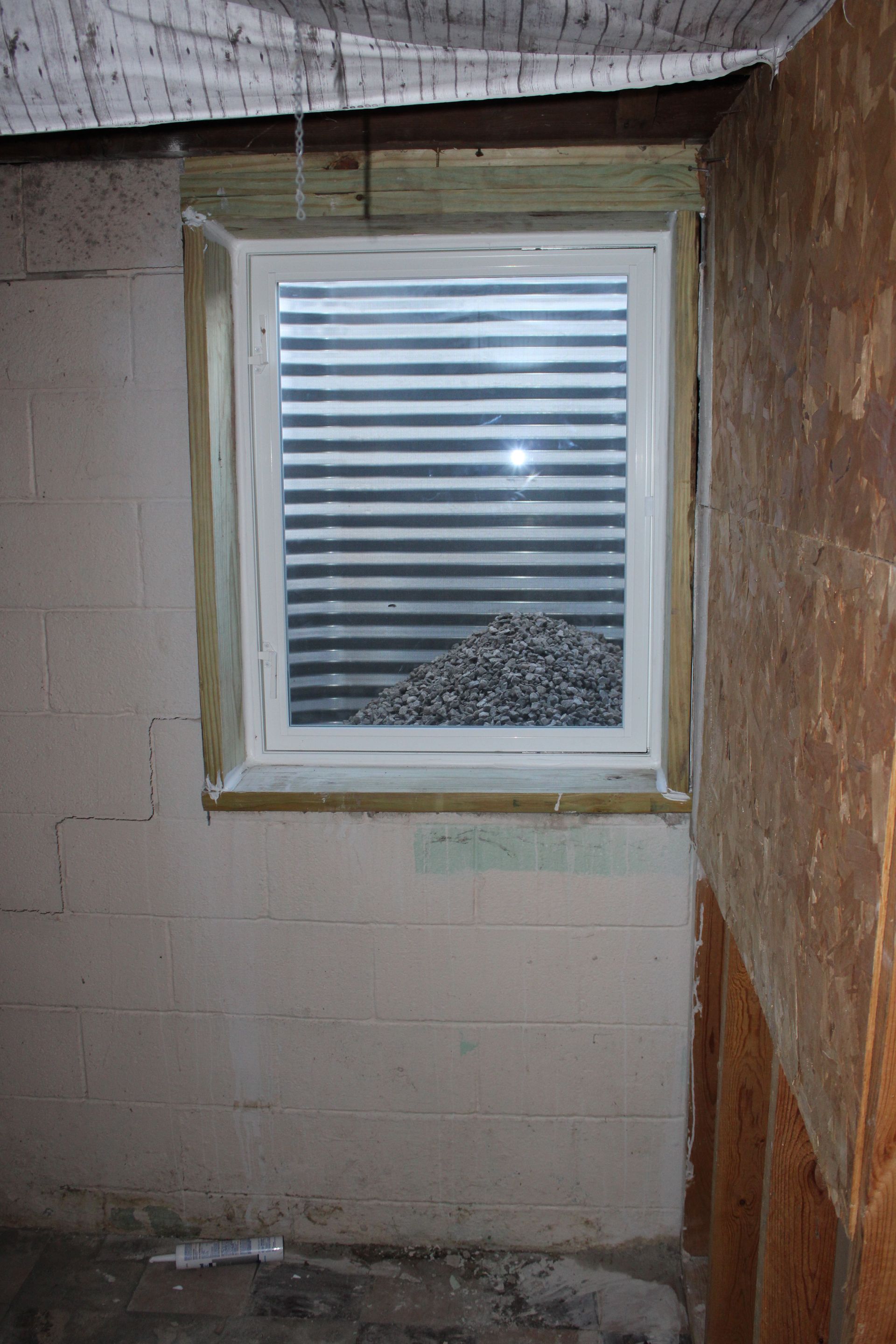 Basement window with gravel visible through the horizontal blinds.