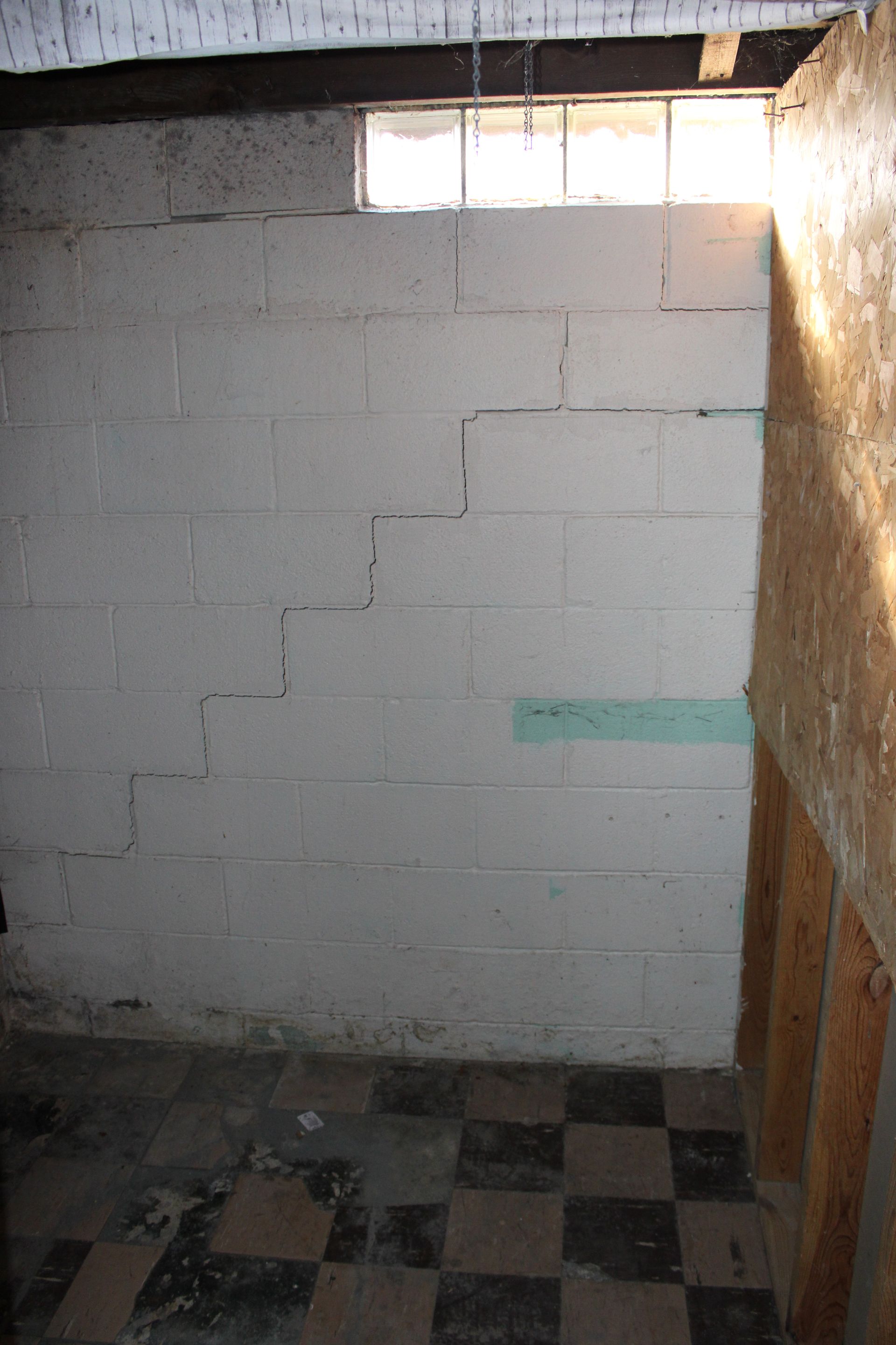 Basement wall with step-like cracks, a small window, and a checkered floor.