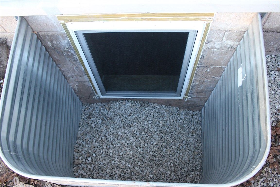 Window well with metal sides and gravel base, outside a basement window.