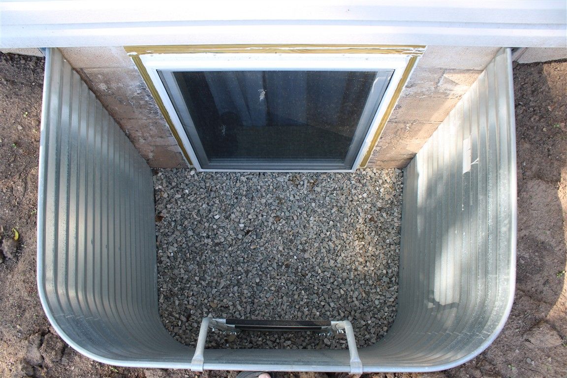 Basement window with gravel in a metal window well.
