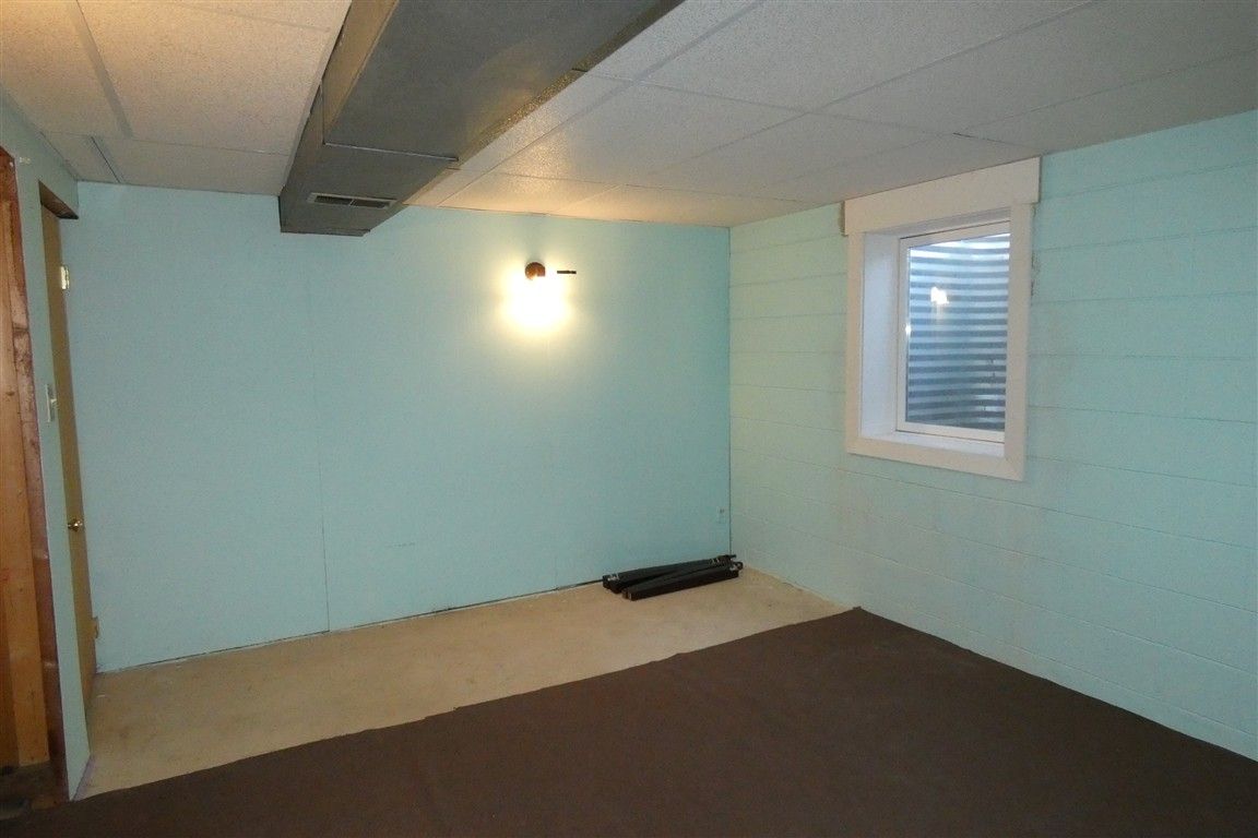 Basement room with blue-green walls, a brown carpeted floor, window, ductwork, and a light fixture.