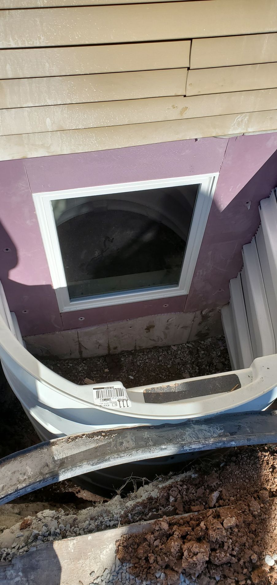 Window well with a white frame and curved bottom section against a light purple wall.