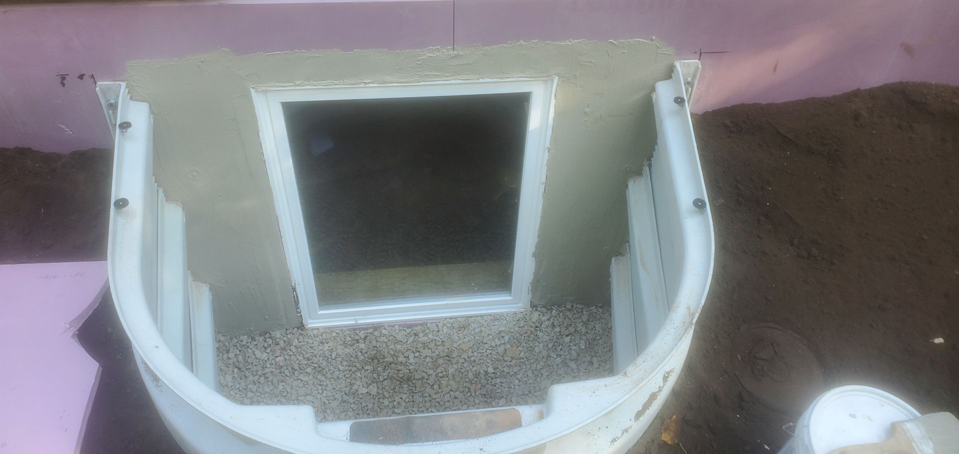 A white plastic structure with a window opening, on a surface with small pebbles.