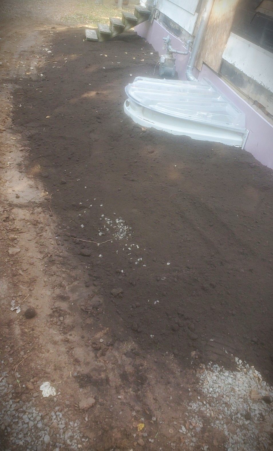 Dark soil covers ground beside a building's white steps and wall, with a concrete border.