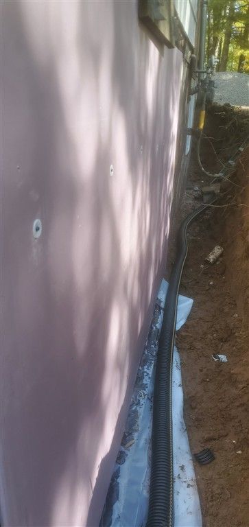 Pink siding with black drainage pipe installed at the foundation of a building.