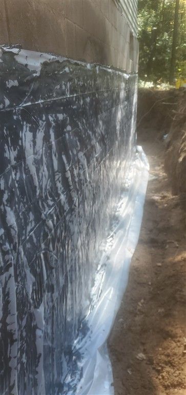 Building foundation wrapped in black waterproof membrane, with a trench of dirt alongside.