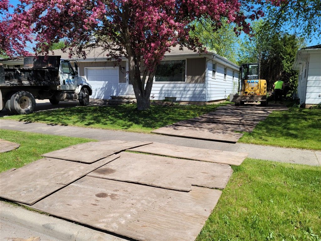 Driveway repair underway at a one-story house with heavy machinery, concrete slabs and a dump truck.