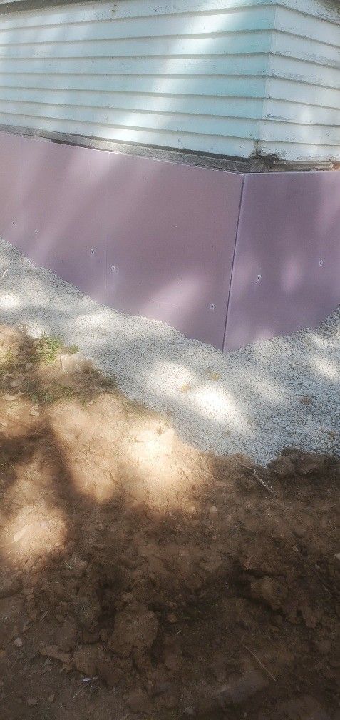 Purple insulation against a building's foundation, covered in gravel. 