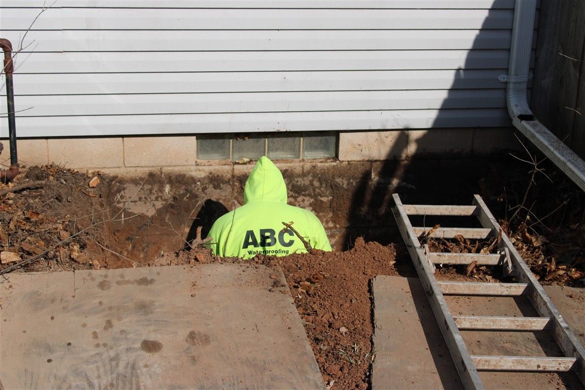 Person in neon jacket in a dug-out hole by a house foundation. 