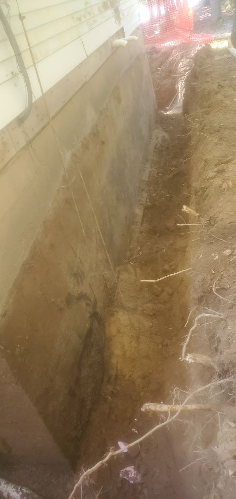 A narrow trench beside a concrete wall, likely part of construction.