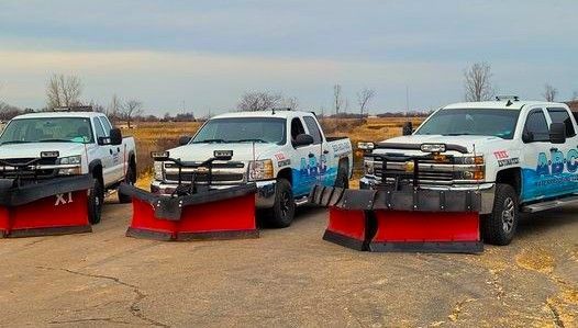 Three pickup trucks with red snowplows lined up outside.