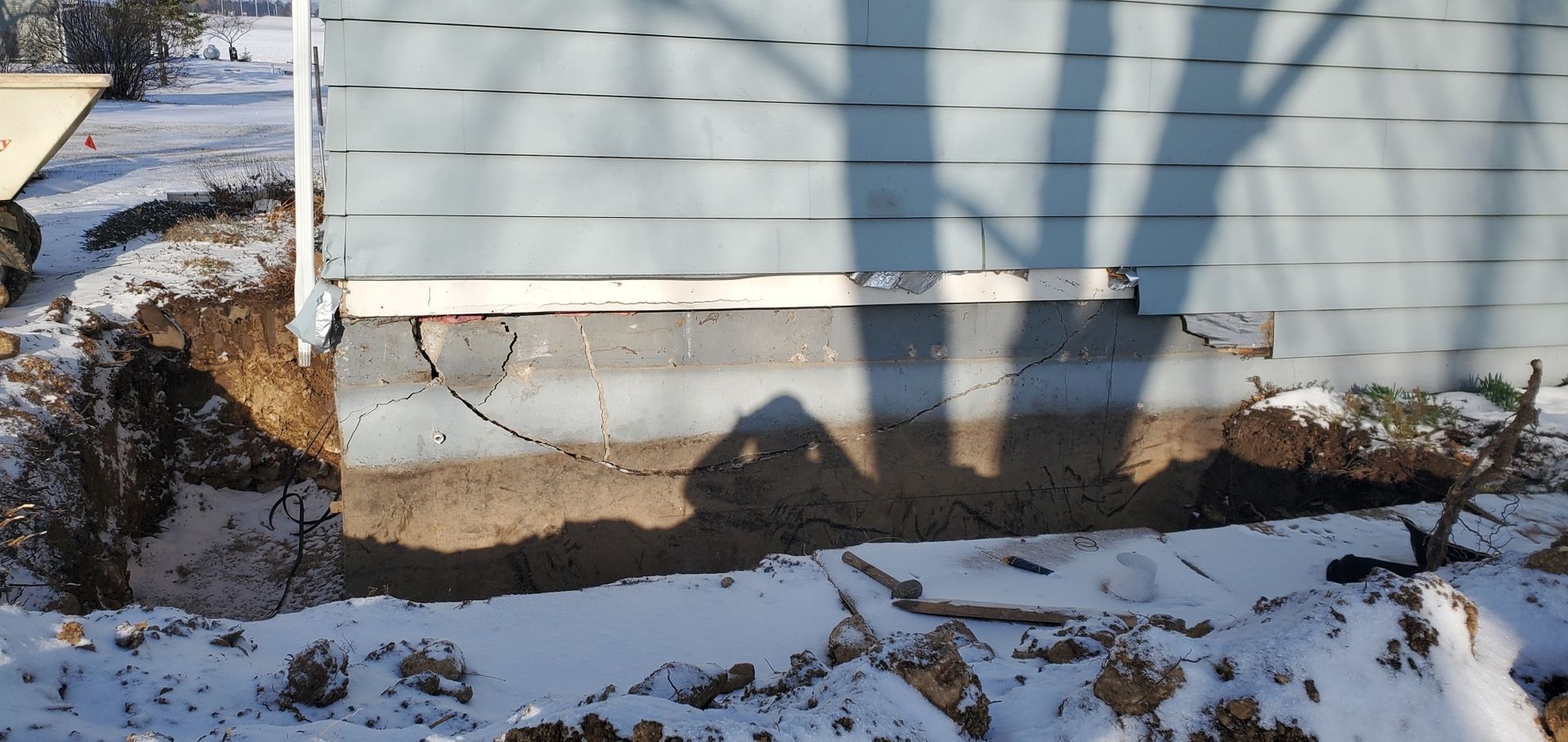 Foundation of a building with cracks, exposed by excavation in snowy conditions.