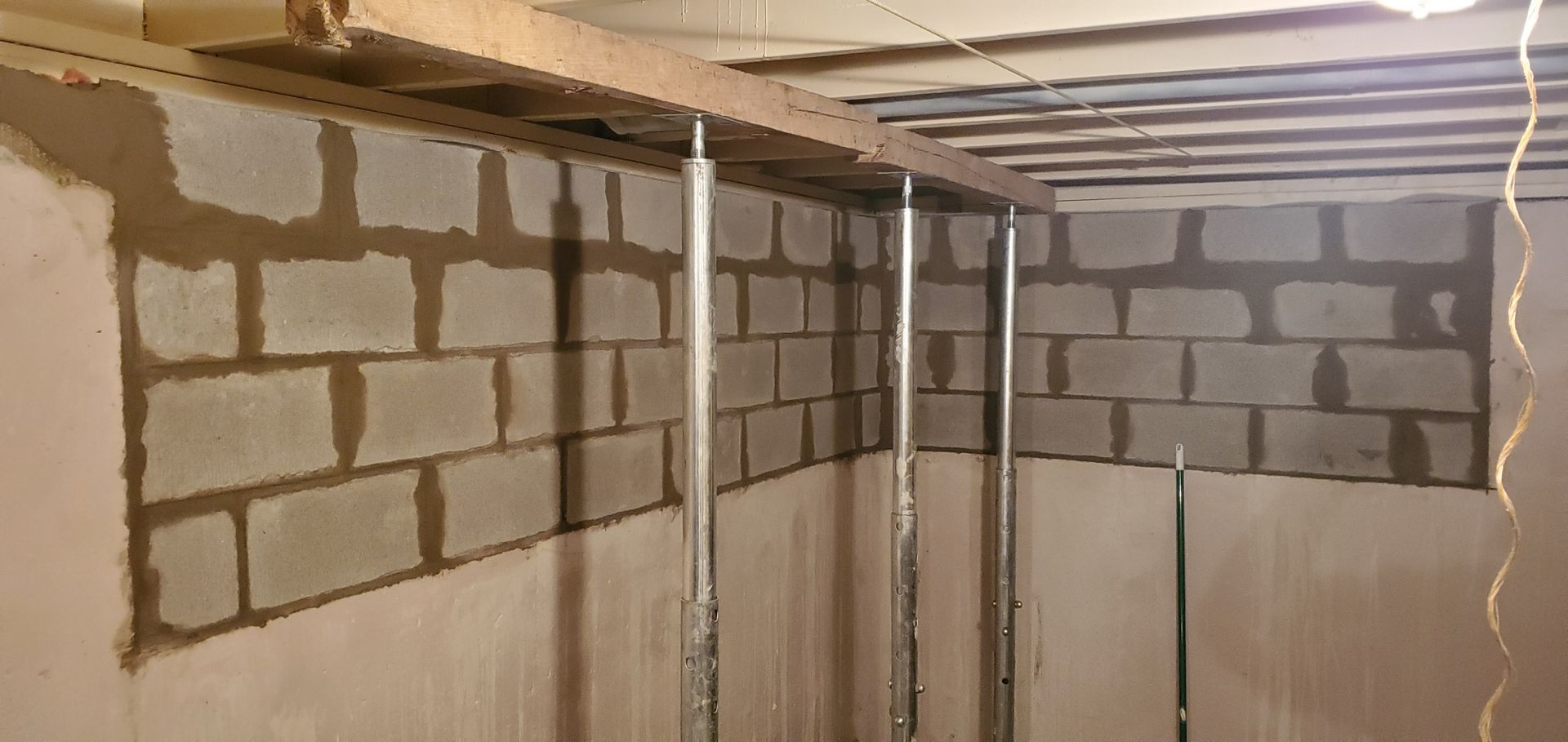 Interior view of a basement, with cinder block walls and support jacks holding up a wooden beam.