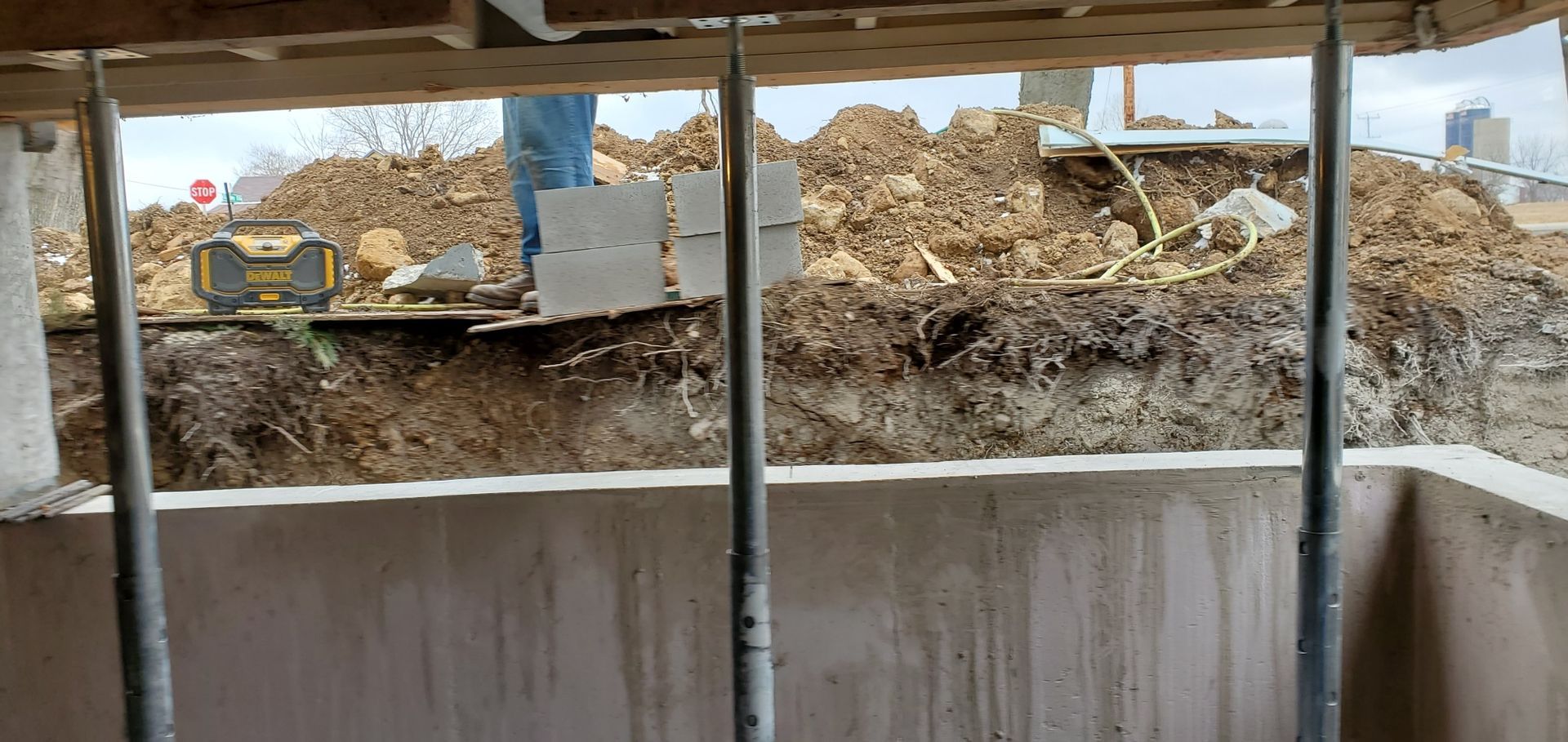 Construction site with dirt pile behind concrete wall and metal support beams.