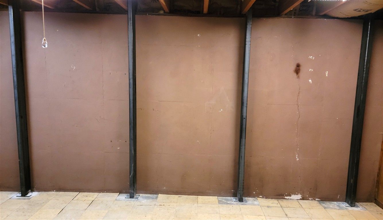 Brown wall with three black support beams in a room with a tiled floor.
