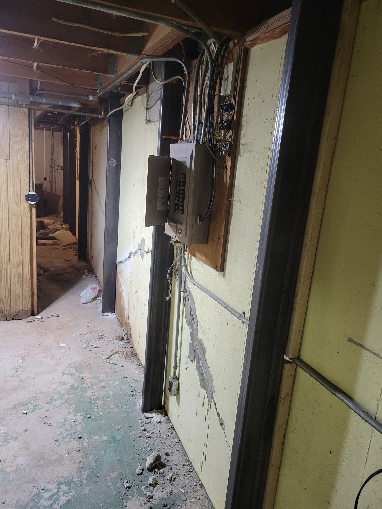 Interior view of a basement hallway with electrical panels on a cracked wall.