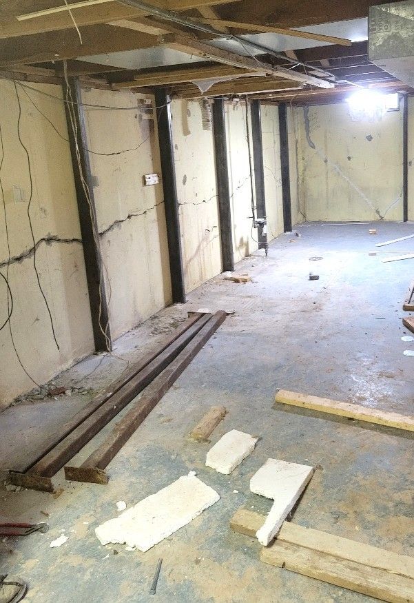 Worker in yellow safety gear cutting foundation wall next to a house with a window.