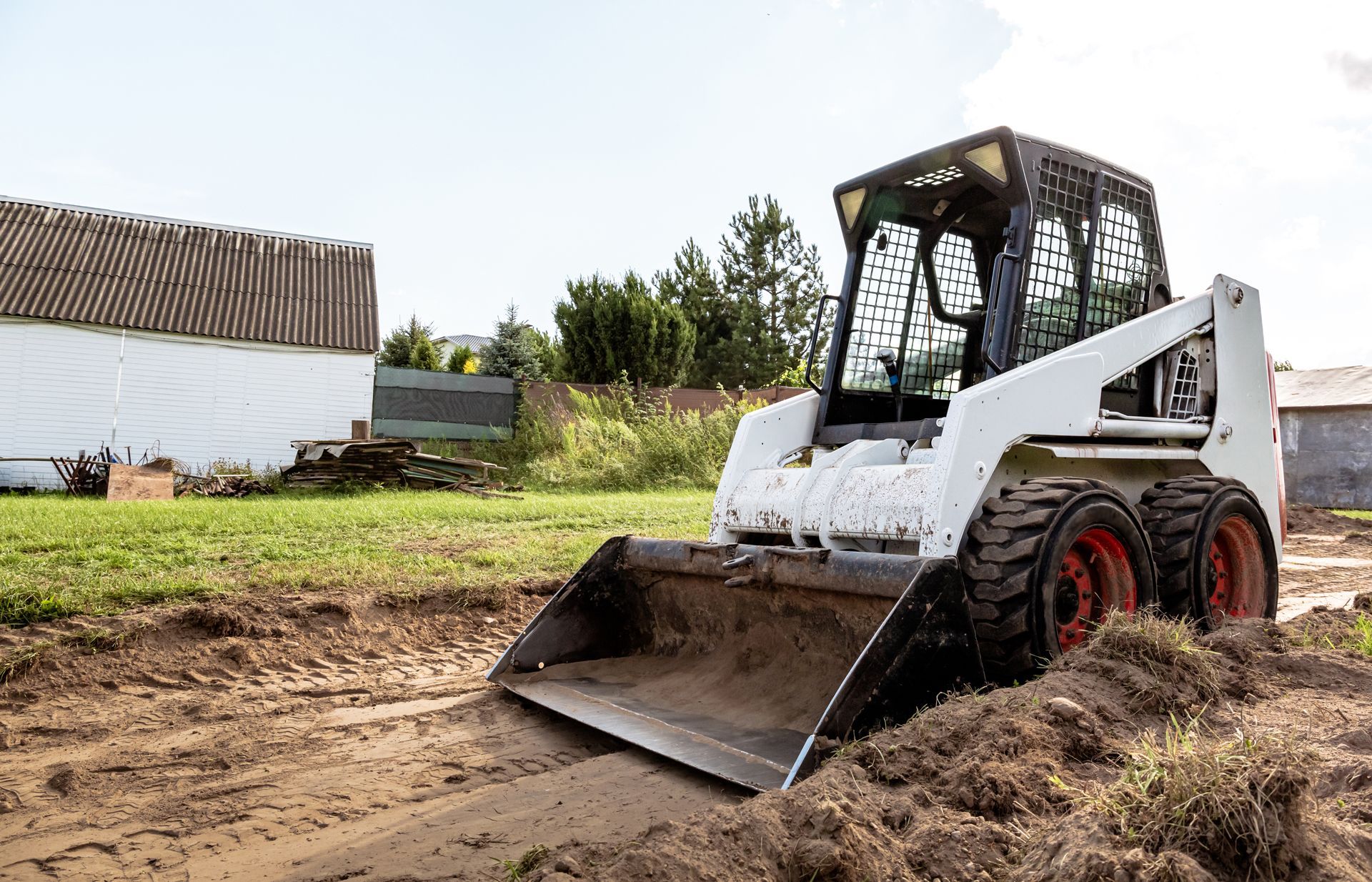White Bobcat skid-steer loader digging in muddy ground on a farm.