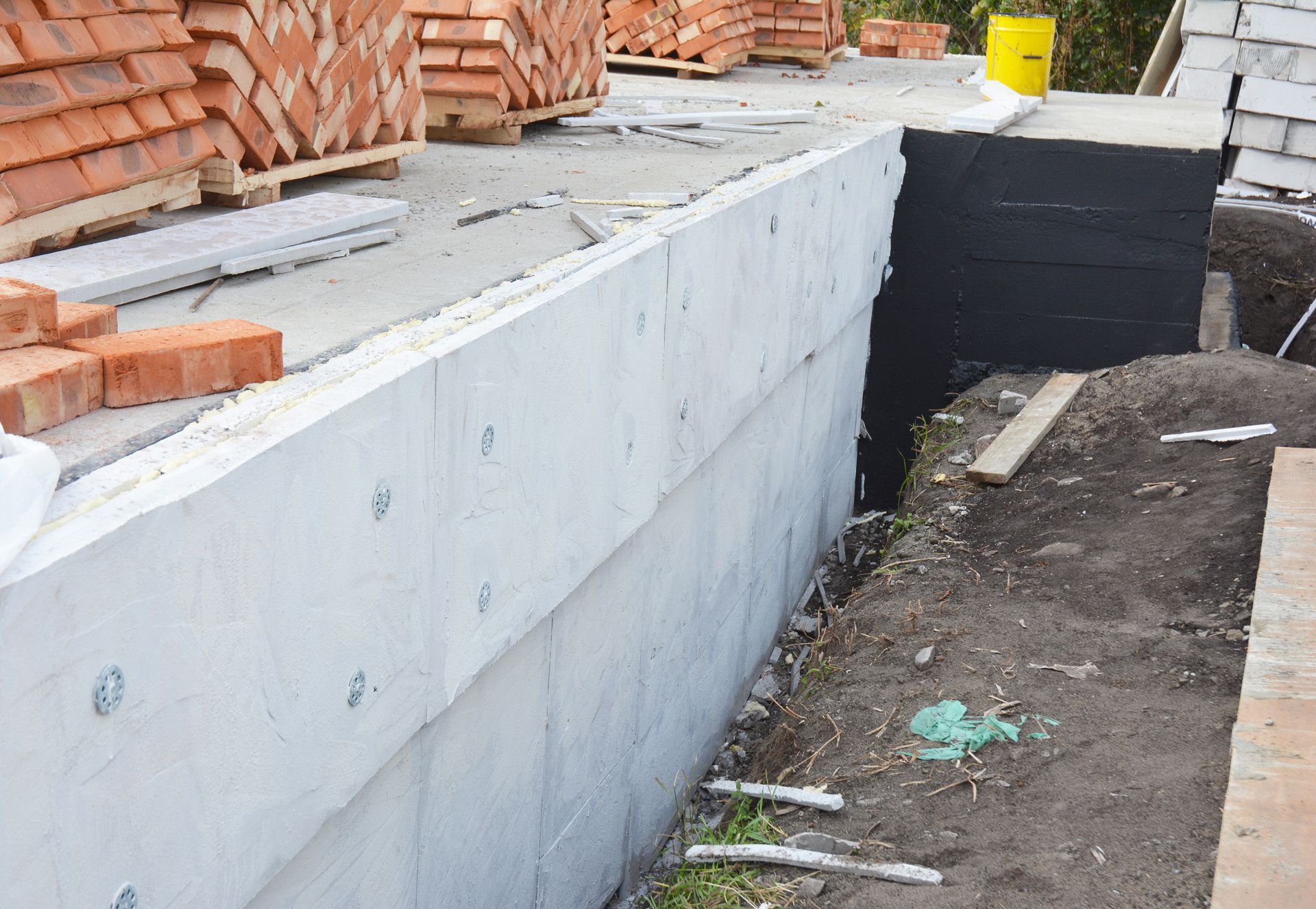 Concrete foundation wall with stacked bricks and excavated soil alongside.