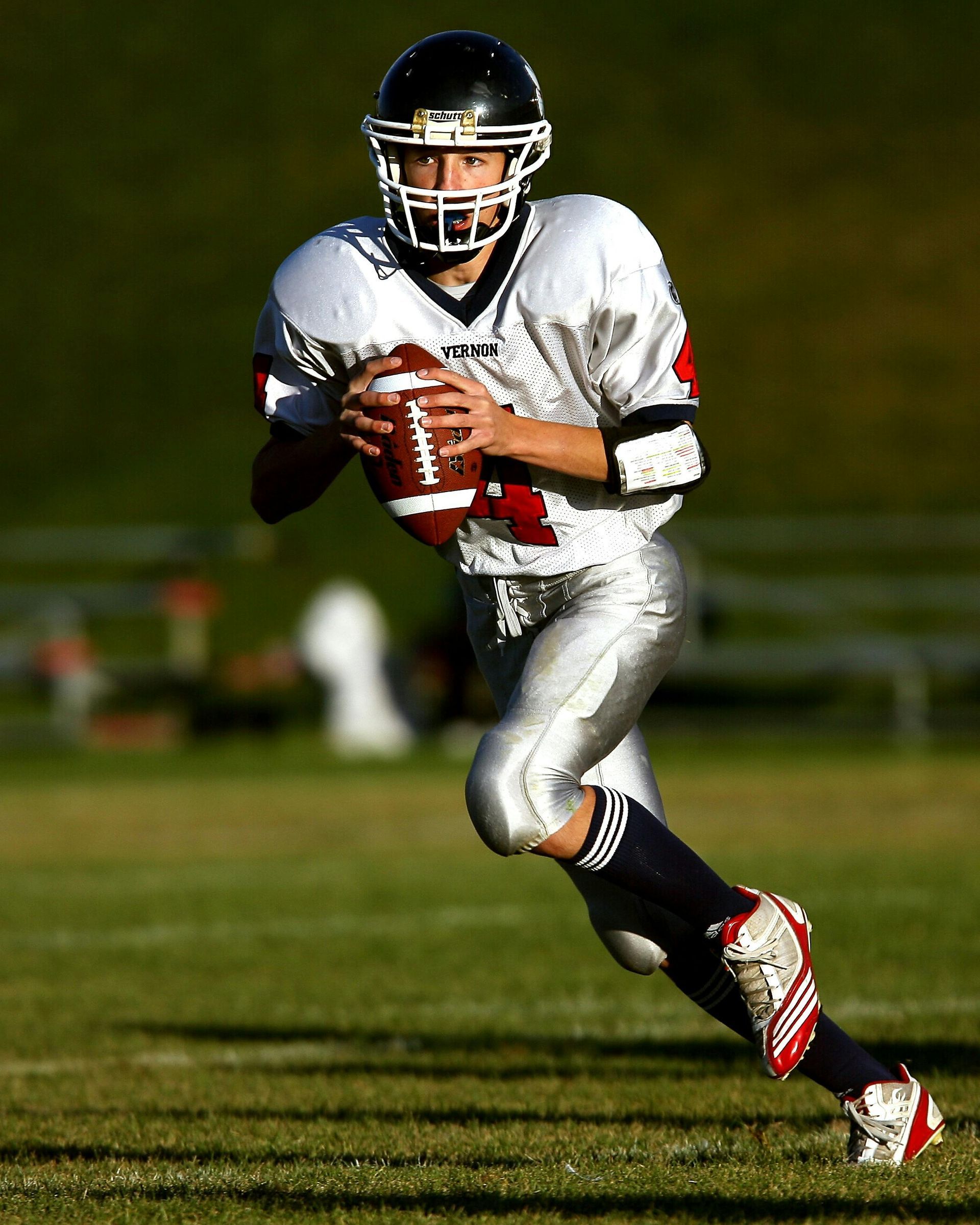 Football player in silver uniform runs with ball on a green field.