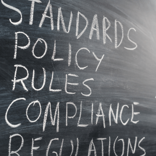 A blackboard with the words standards policy rules compliance regulations written in white chalk