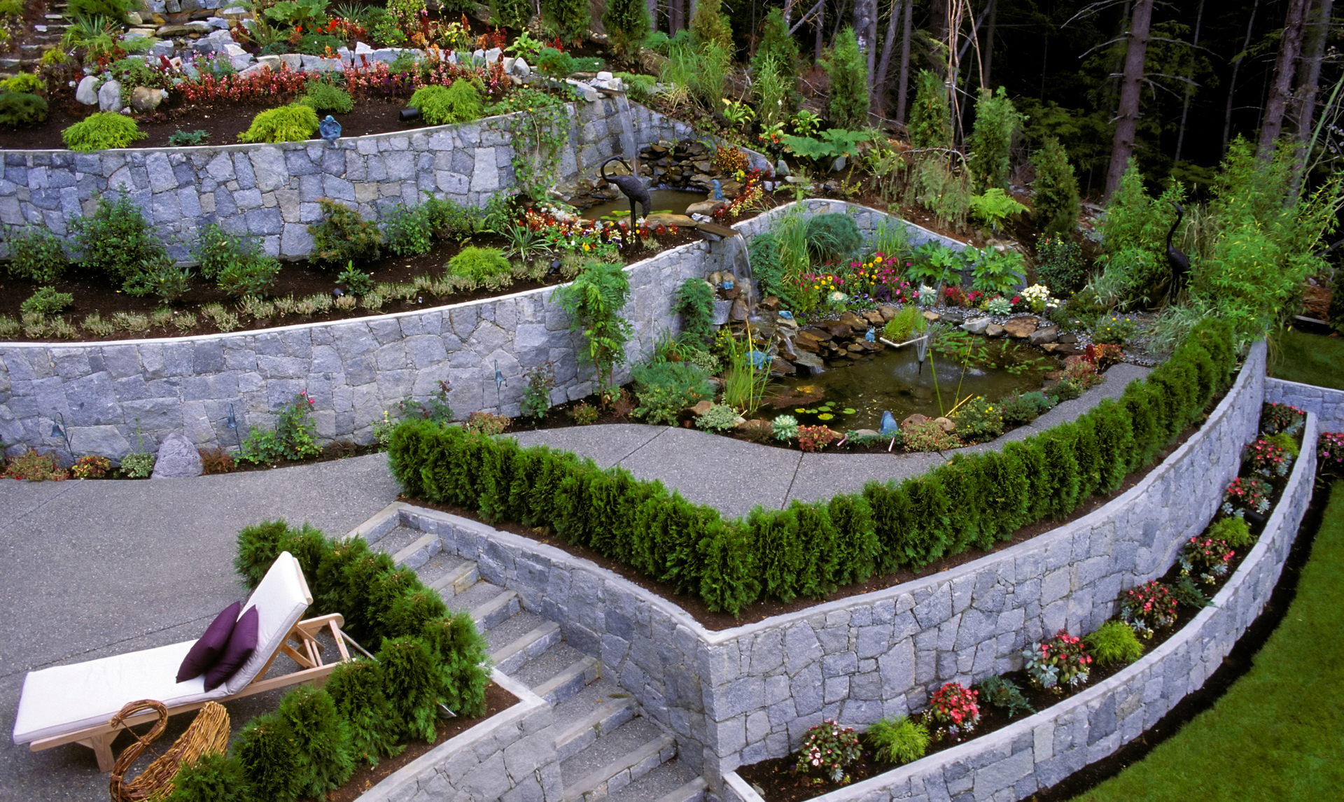 Multi-tiered garden with stone walls, stairs, pond, and various plants.