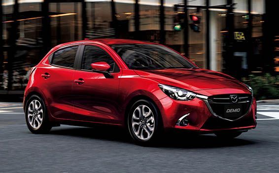 Red Mazda 2 hatchback car driving on a city street.