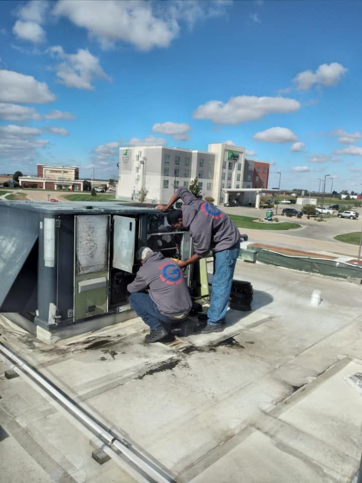 Two men are working on an air conditioner on the roof of a building.