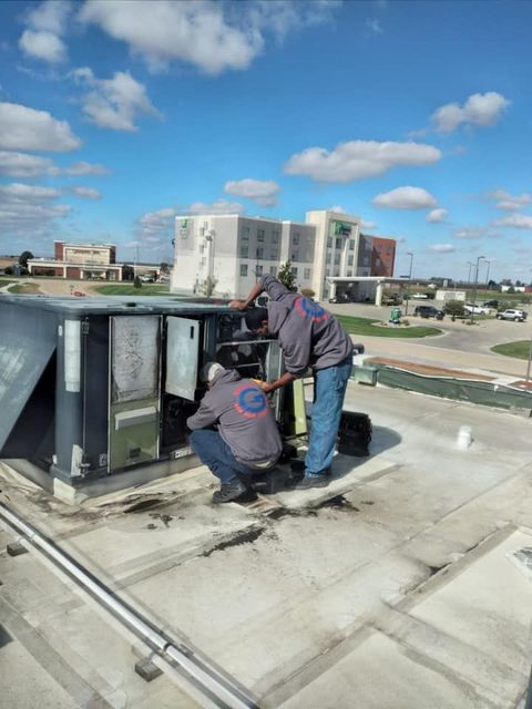 Two men are working on an air conditioner on the roof of a building.