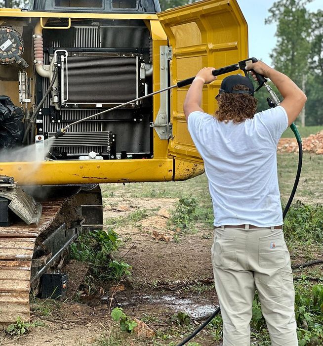 A man is cleaning a yellow excavator with a hose
