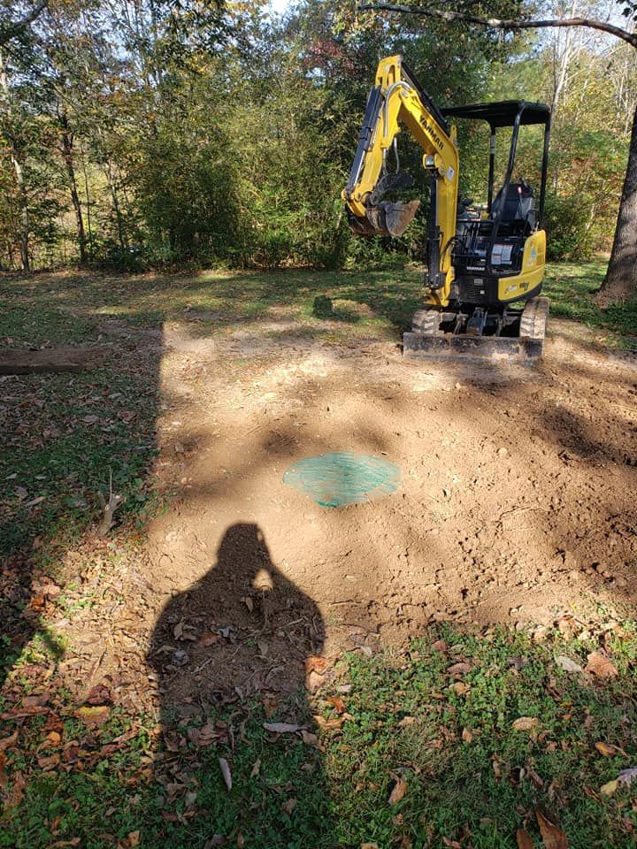 A yellow excavator is digging a hole in the dirt in a yard.