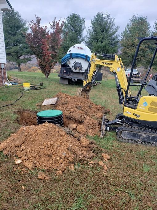 A yellow excavator is digging a hole in a yard next to a septic tank.