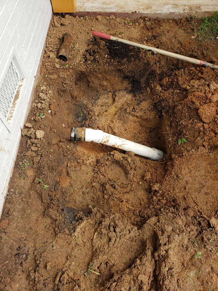 A white pipe is laying in the dirt next to a shovel.
