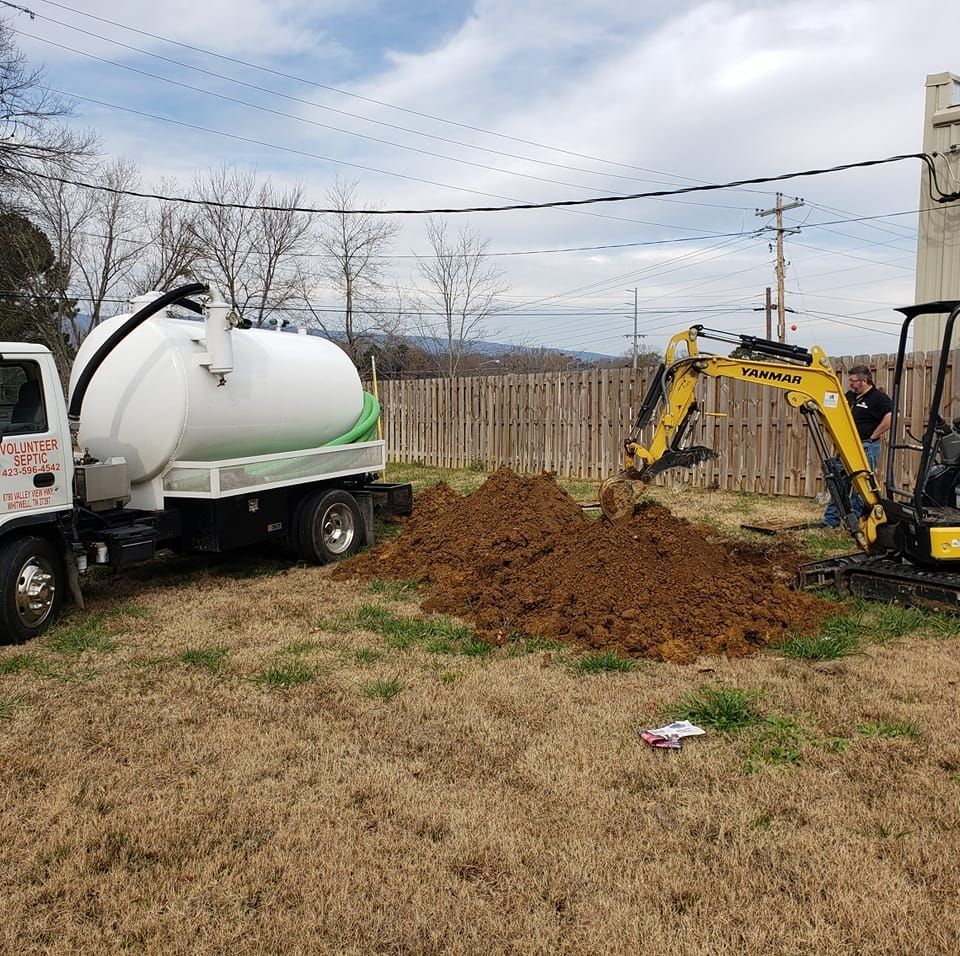 A yellow excavator is digging a hole in the ground next to a vacuum truck.
