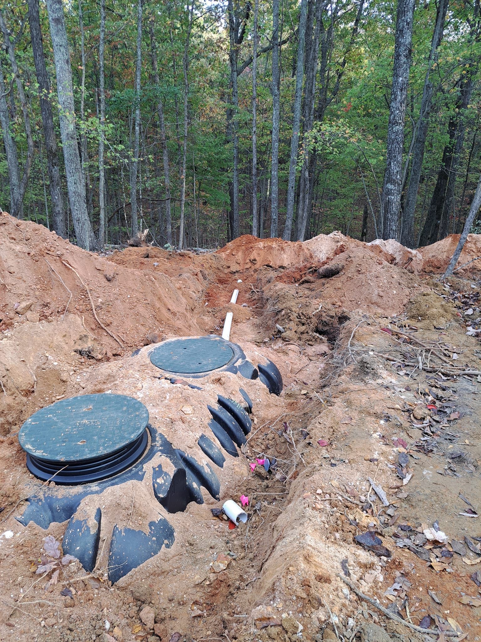 A septic tank is sitting in the middle of a dirt field in the woods.