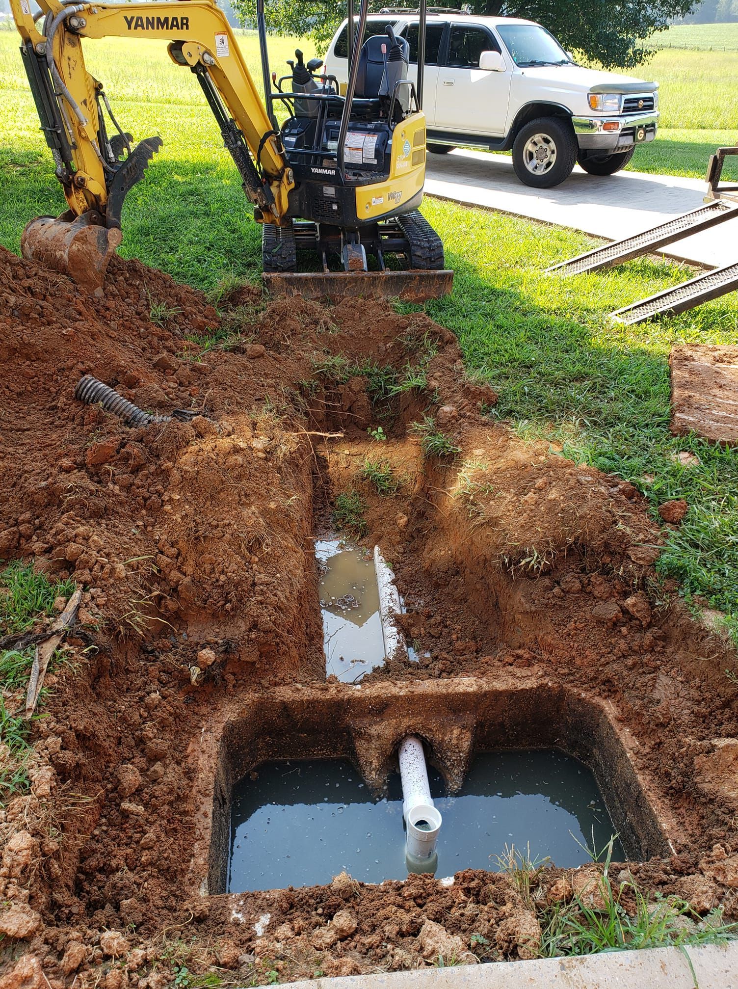 A yellow excavator is digging a hole in the ground next to a white truck.