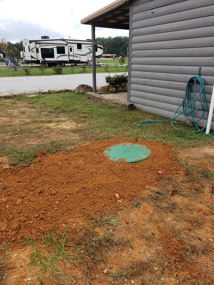 A septic tank is sitting in the dirt in front of a log cabin.
