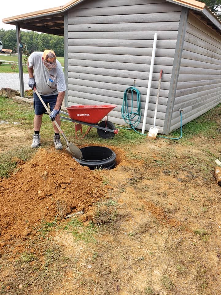 A man is digging a hole in the ground next to a wheelbarrow.