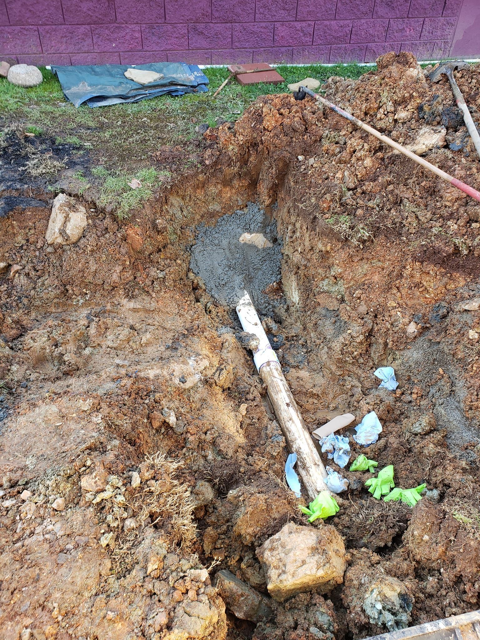 A shovel is laying in the dirt next to a pipe.