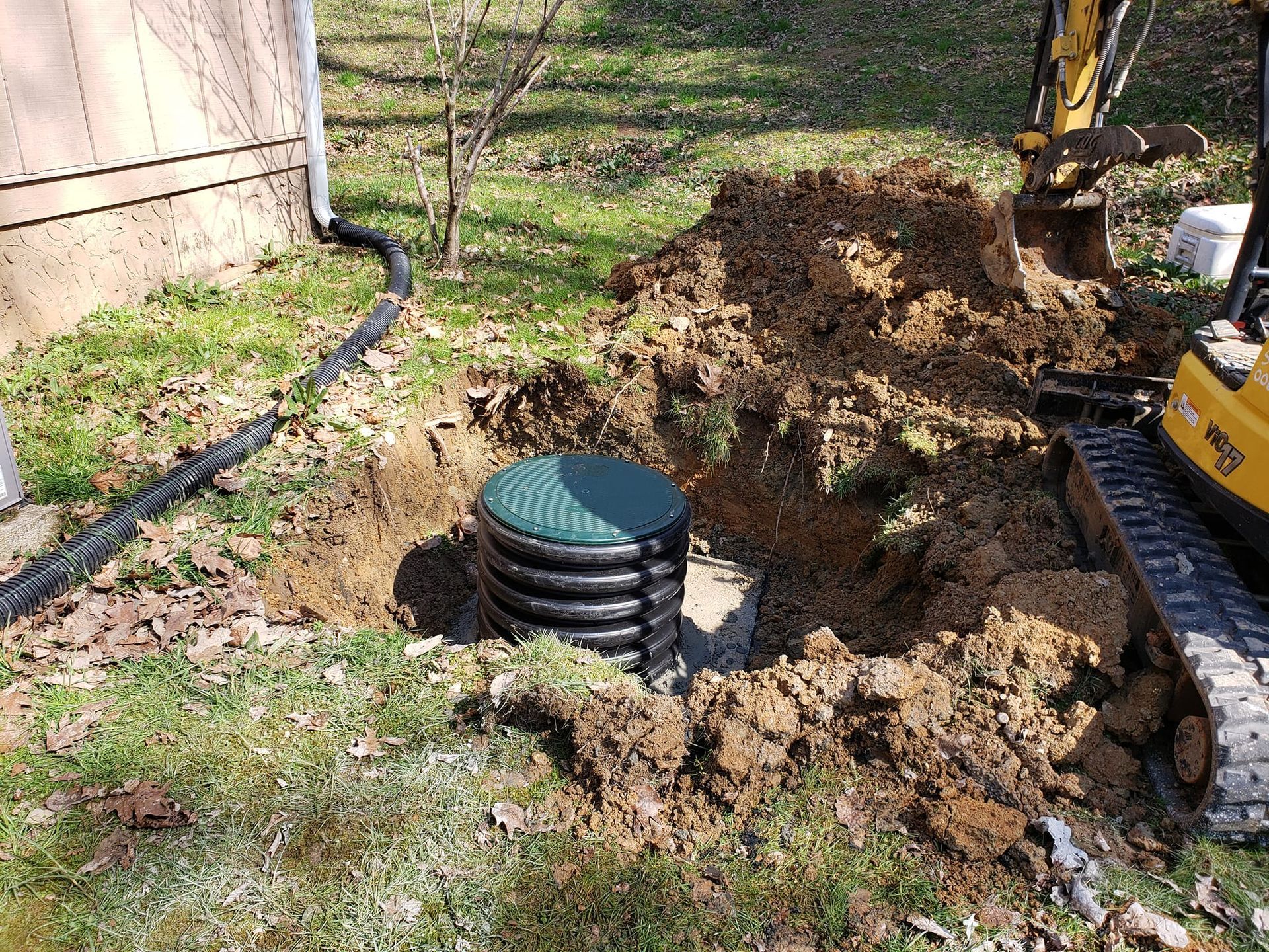 A yellow excavator is digging a hole in the ground to install a septic tank.