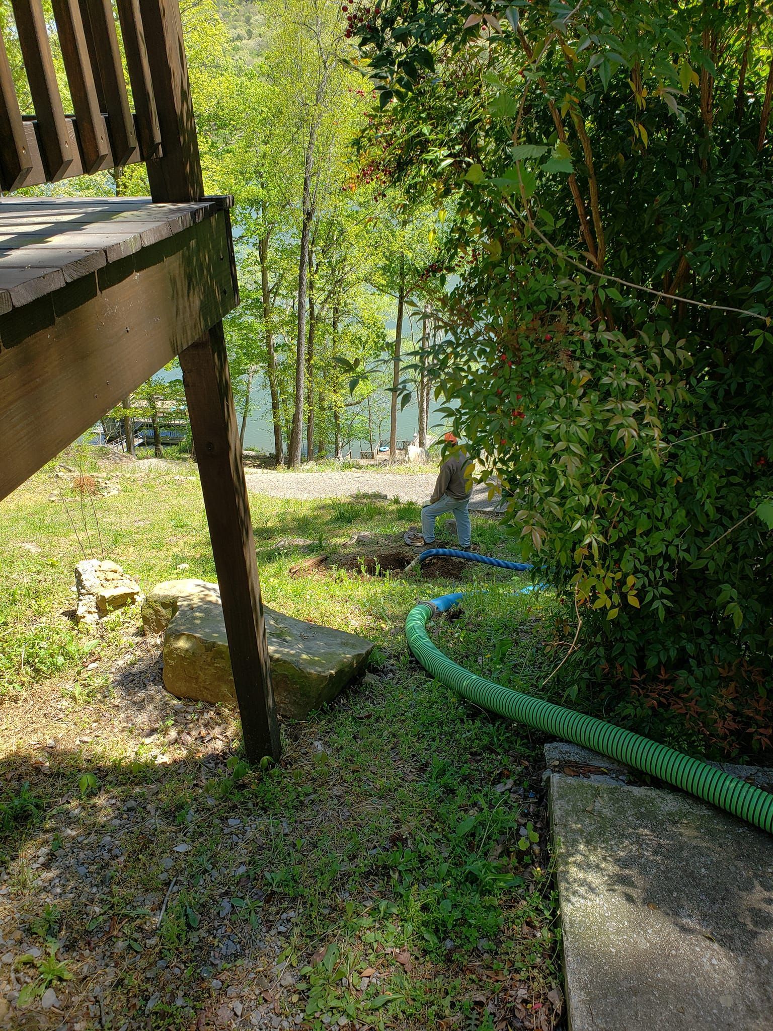 A green hose is laying in the grass next to a wooden deck.